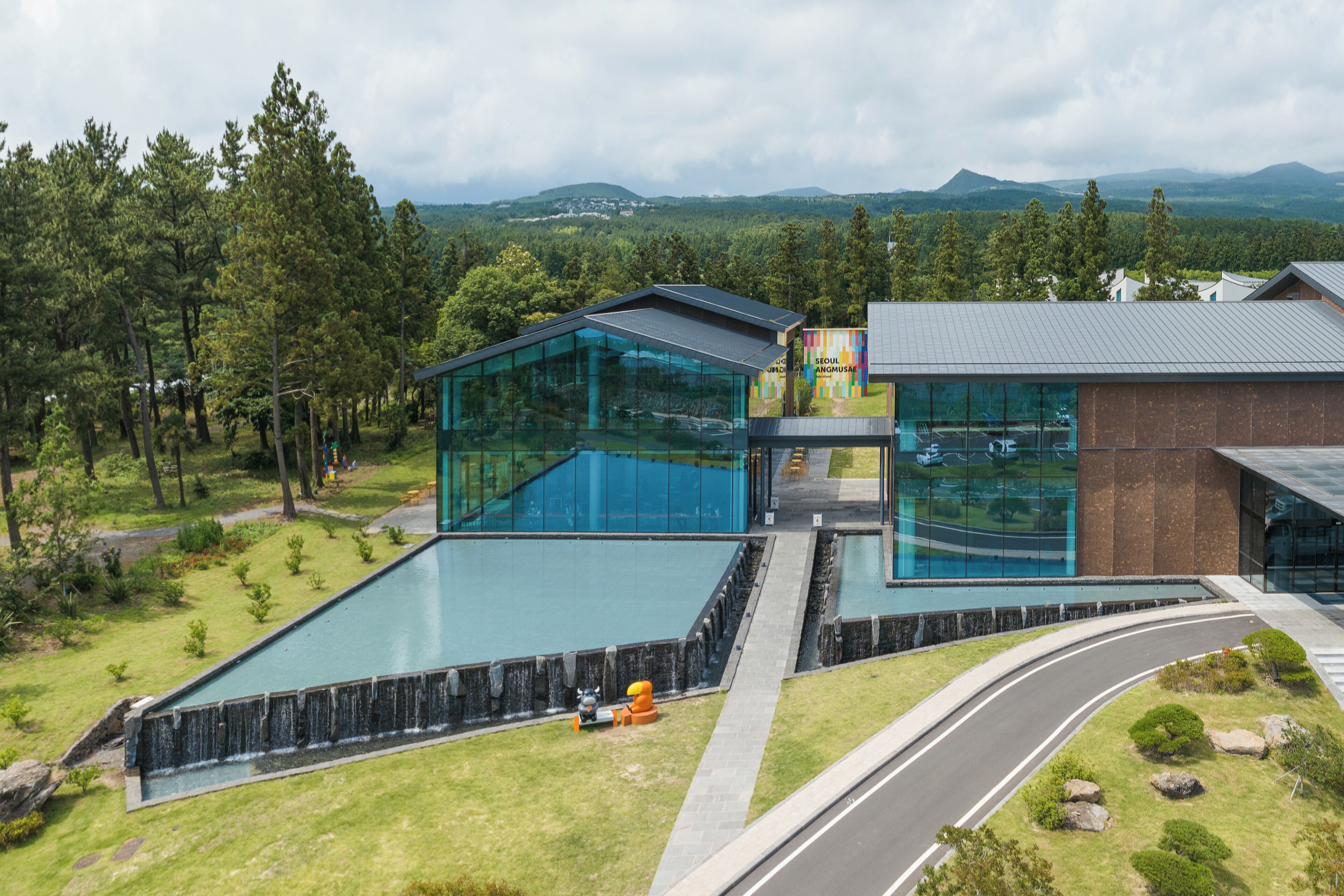A modern building with a glass facade, a swimming pool, and a road leading to it.