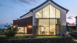 Una casa moderna con amplios ventanales de vidrio, un muro de piedra frontal e interior bien iluminado.