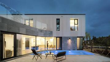 A modern house with a glass-enclosed balcony, a swimming pool, and a patio with outdoor furniture.