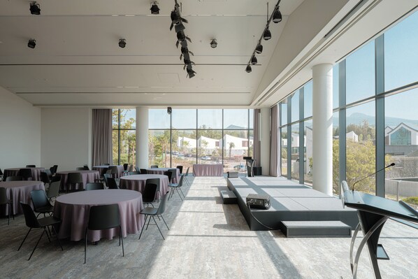 Une salle de conférence dotée de tables rondes, d’une scène et de grandes fenêtres donnant sur des bâtiments et des montagnes.