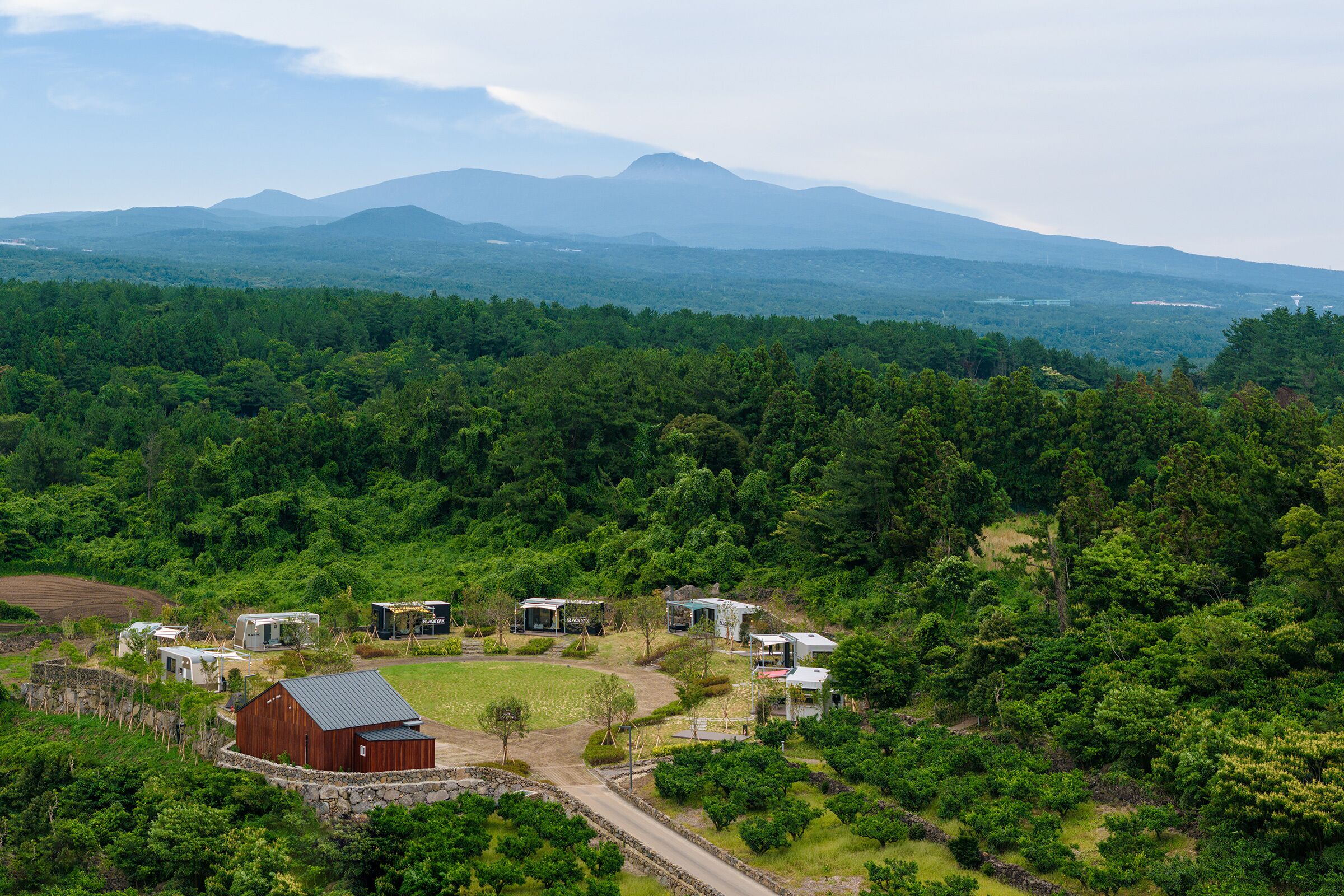 A rural property with multiple buildings, a large barn, and a forested landscape with mountains in the background.