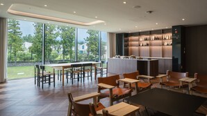 Un comedor moderno con mesas y sillas de madera, una zona de bar con estantes llenos de botellas, y amplias ventanas que ofrecen vistas al exterior.