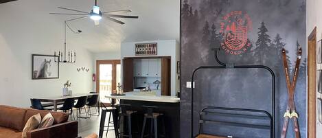 A modern living room with a dining area, a bar, and a ski-themed wall.