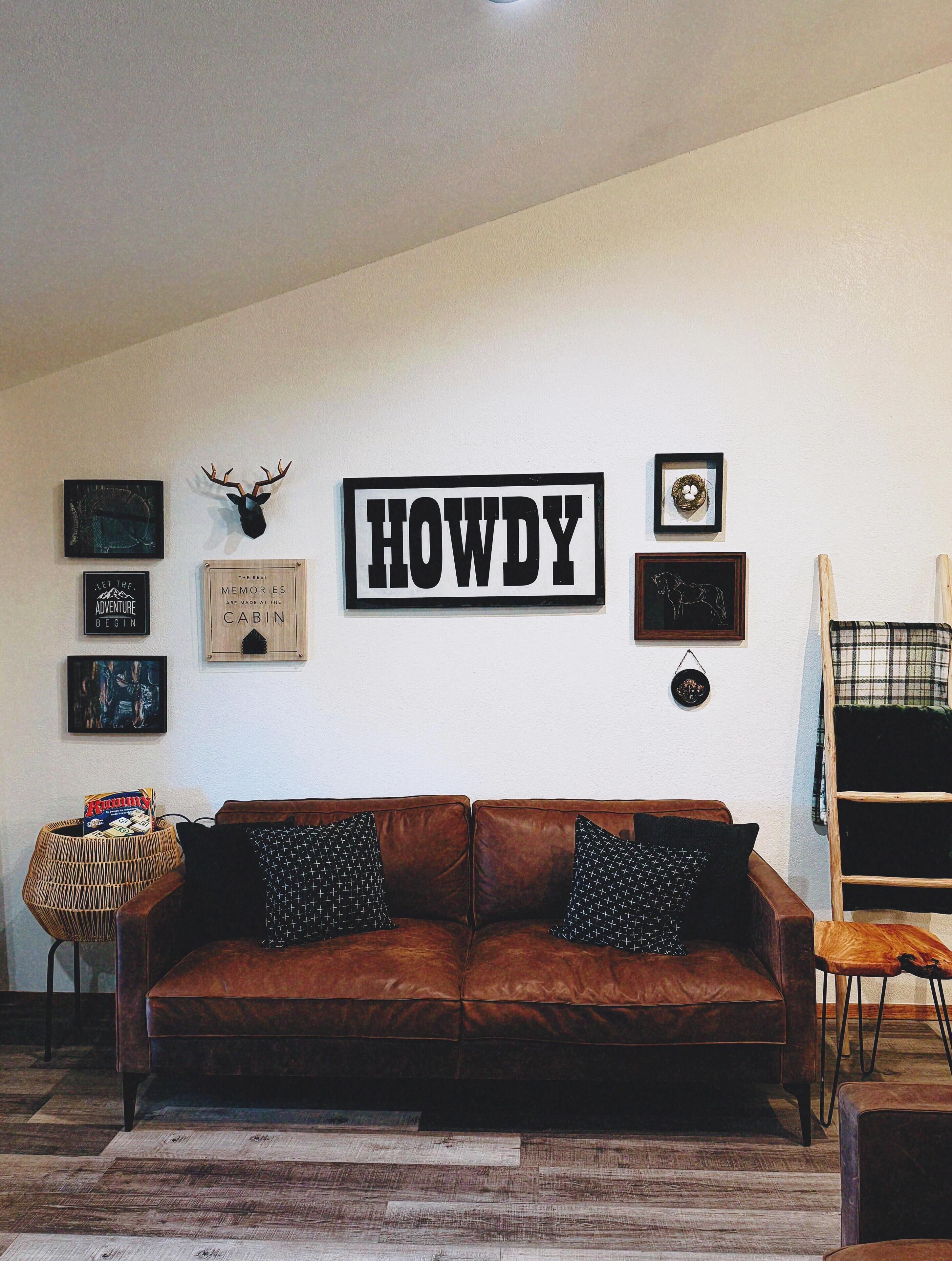 A living room with a brown leather couch, a wooden ladder, and various framed pictures on the wall.
