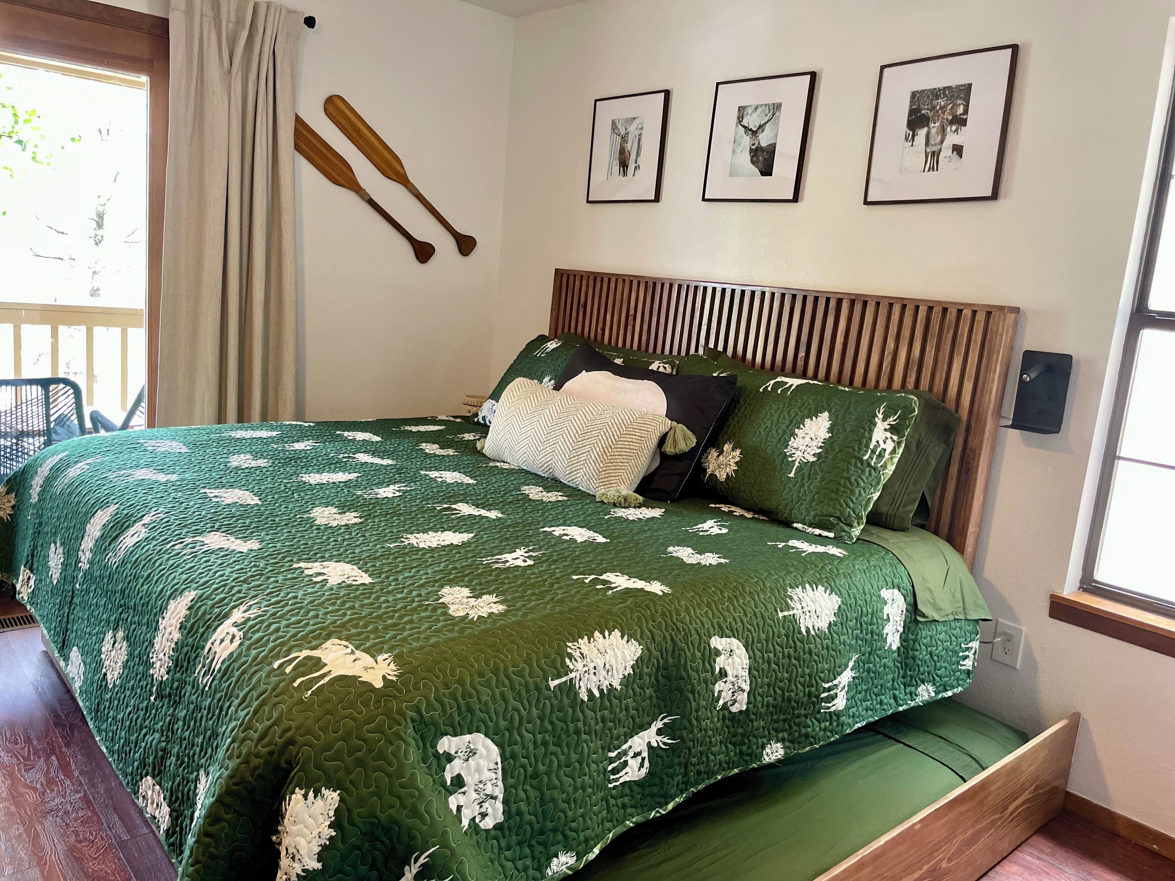 A bedroom with a green quilted bedspread, wooden headboard, and three framed pictures on the wall.