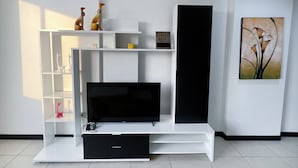 Ein modernes Wohnzimmer mit Flachbildfernseher, weißen Regalelementen und minimalistischer Einrichtung.