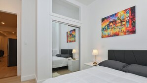A hotel room with a large bed, a nightstand with a lamp, a mirror, and a painting on the wall. - Elegant 4BR Luxury Duplex in chic Upper West Side (New York)