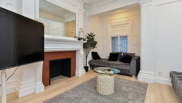 A living room with a fireplace, a flat-screen TV, a grey sofa, and a coffee table. - Elegant 4BR Luxury Duplex in chic Upper West Side (New York)