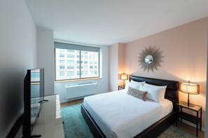 Habitación de hotel con una cama, televisor, ventana, espejo instalado en la pared y dos lámparas de noche.