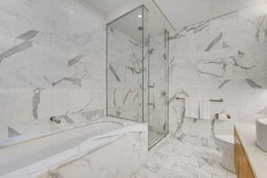 Ein modernes Badezimmer mit einer gläsernen Duschkabine, einer freistehenden Badewanne und einem WC mit Handtuchhalter.