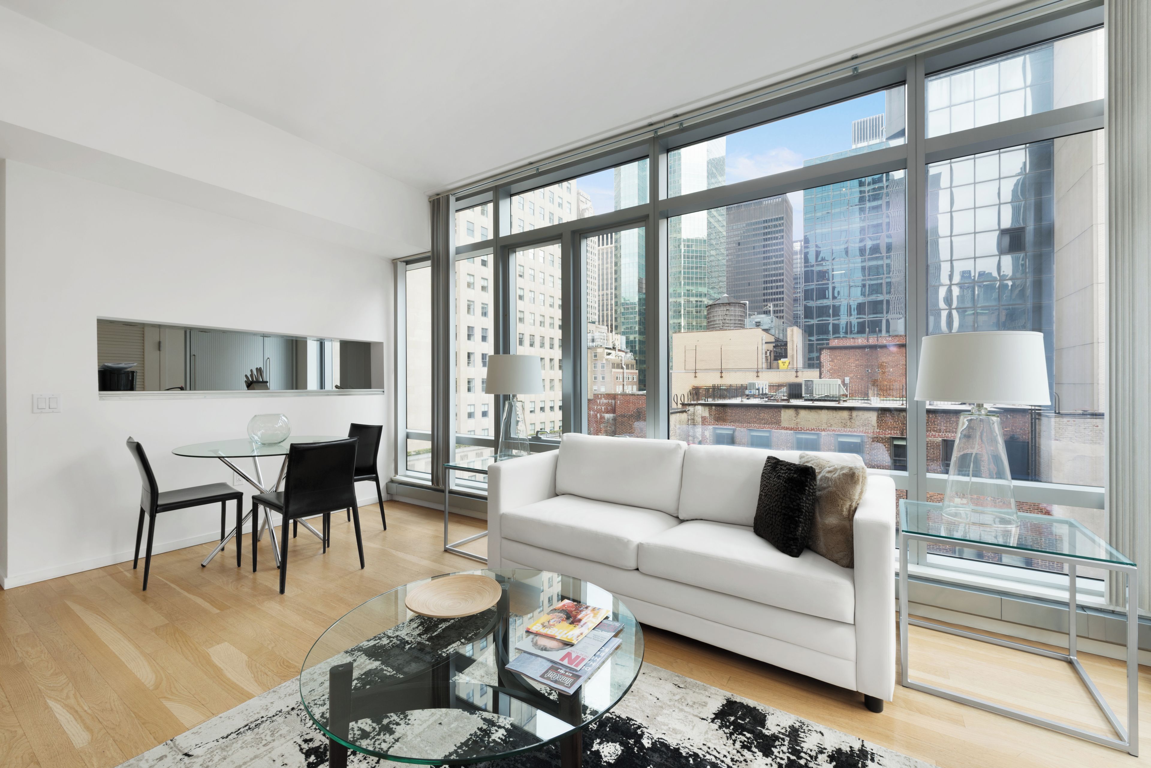 A modern living room with a glass coffee table, a white sofa, and a dining area with a glass table and chairs.