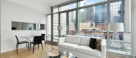 A modern living room with a glass coffee table, a white sofa, and a dining area with a glass table and chairs.