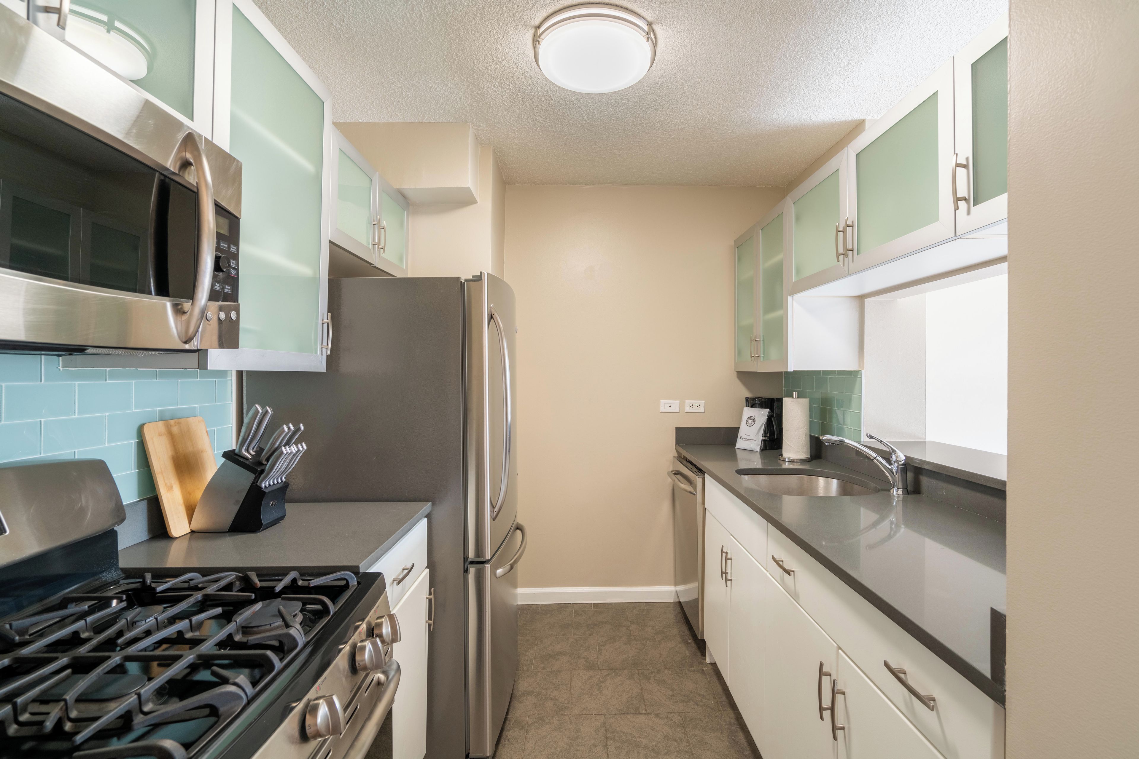 A modern kitchen with stainless steel appliances, light green cabinets, and a beige tiled backsplash.
