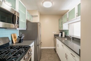 A modern kitchen with stainless steel appliances, light green cabinets, and a beige tiled backsplash.