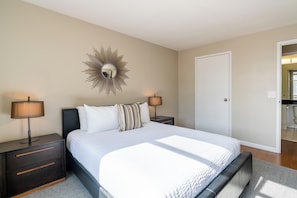 A bedroom with a large bed, two bedside tables with lamps, a wall-mounted mirror, and a door to another room. - Classic NYC Living | Upper West Side | Rooftop (New York)