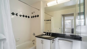 Un baño con bañera, lavamanos e inodoro. Hay una cortina de ducha, un espejo y una ventana.
