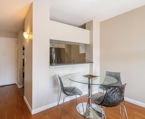 A dining area with a glass table and chairs, a stainless steel refrigerator, and a wall-mounted shelf. - Classic NYC Living | Upper West Side | Rooftop (New York)