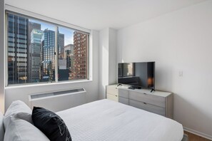 Une chambre moderne avec une grande fenêtre, un lit, une télévision et une commode.