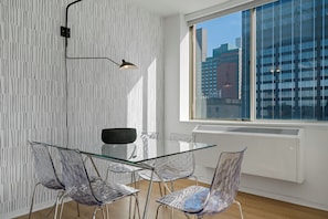 A modern dining area with a glass table and chairs, a patterned wall, and a view of buildings through a large window.