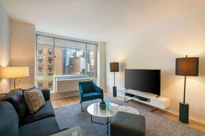 Un salon moderne comprenant un canapé, un fauteuil, une table basse, un téléviseur et un lampadaire.