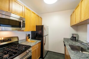 Eine kompakte Küche mit Holzausstattung, Edelstahlgeräten – darunter Mikrowelle, Backofen und Kühlschrank – einer Granit Arbeitsplatte und einem integrierten Spülbecken.