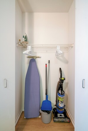 Un espace dédié à la lessive, équipé d’une planche à repasser, d’un aspirateur et d’une serpillière.