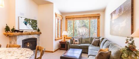 A cozy living room with a fireplace, a large window, a sofa, and a dining table.