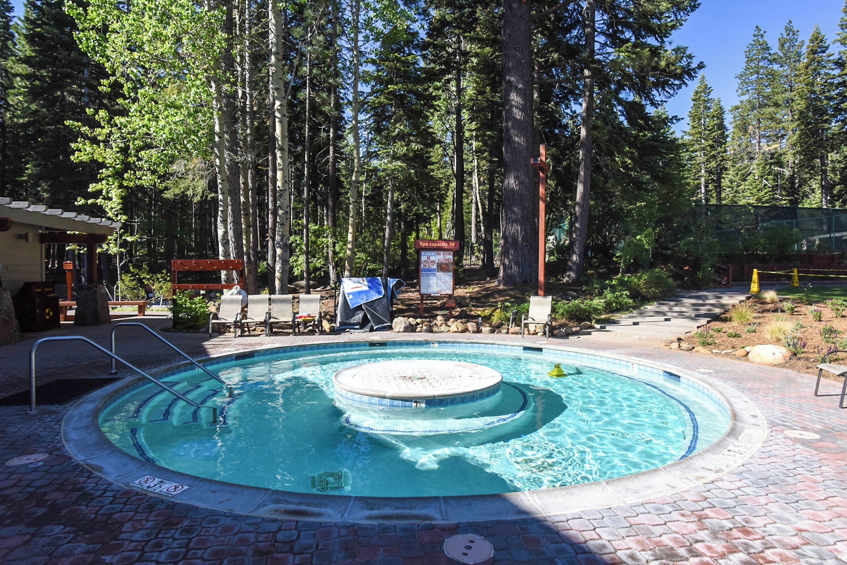 Un jacuzzi rond, entouré d’une terrasse en briques, avec une plateforme en bois et des chaises longues à l’arrière-plan.