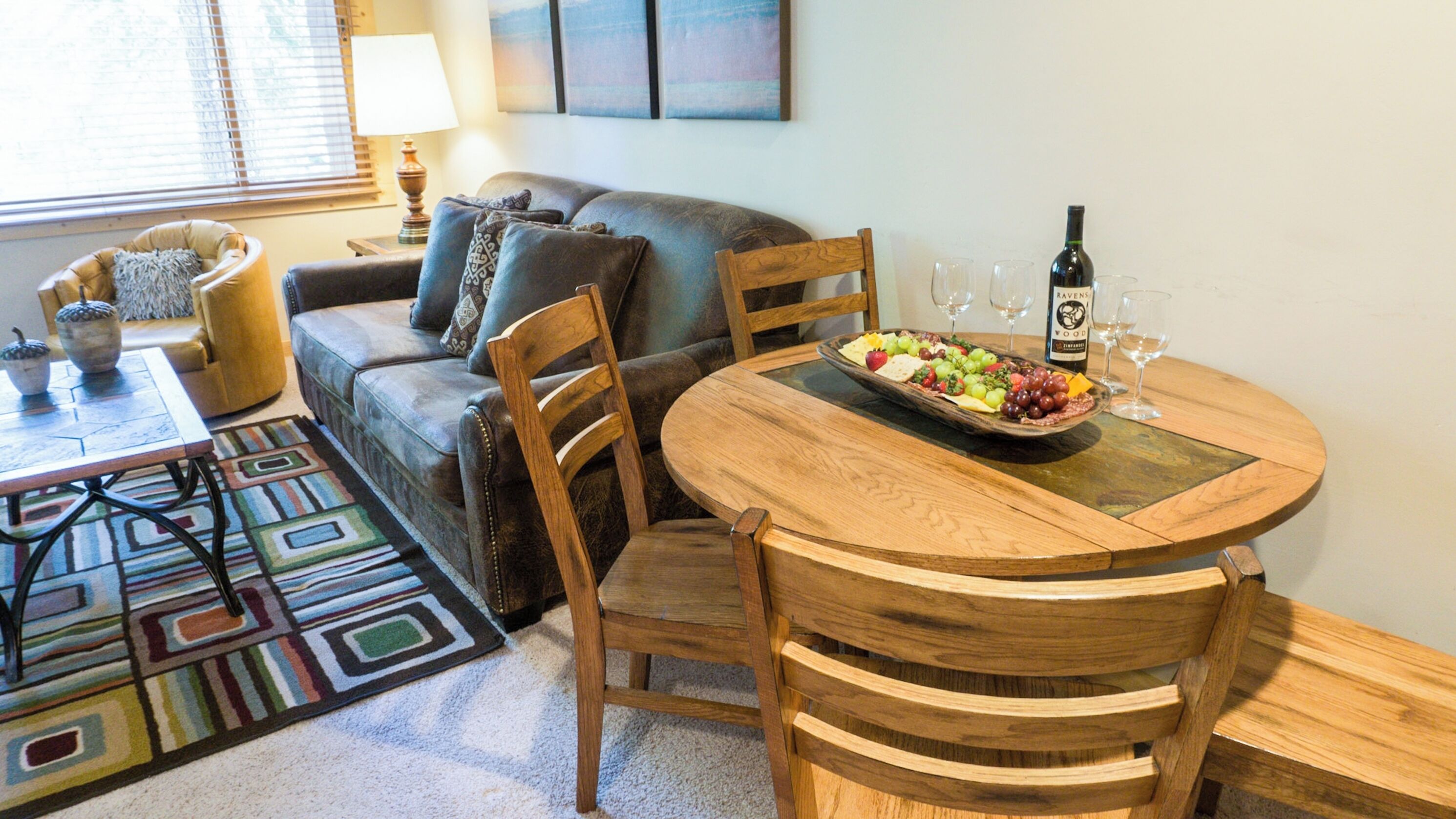 Un salón acogedor con un sofá, una mesa de comedor de madera con sillas, un tapete decorativo y una botella de vino sobre la mesa.