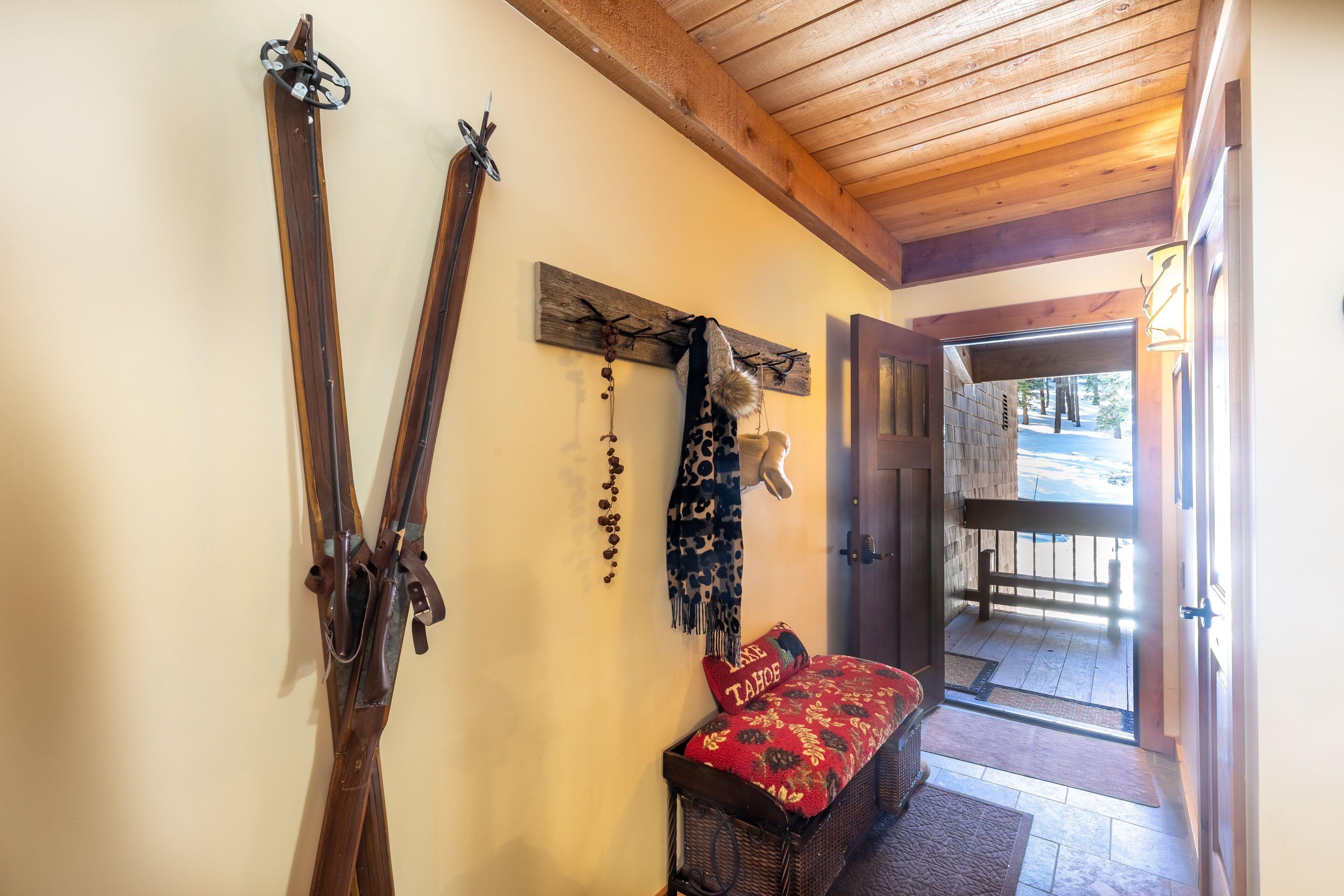 A room with skis leaning against the wall, a bench with a red blanket, and a wooden ceiling.