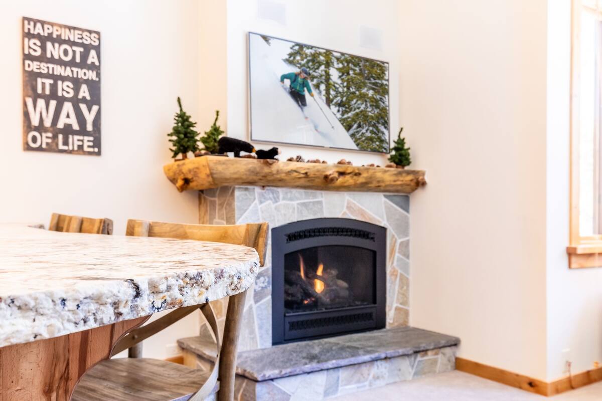 A cozy room with a stone fireplace, a wooden table, and a framed picture of a skier.