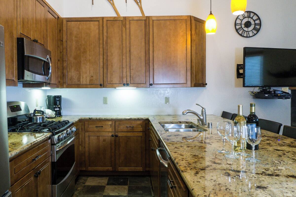 A kitchen with wooden cabinets, a stainless steel refrigerator, a gas stove, and a sink.