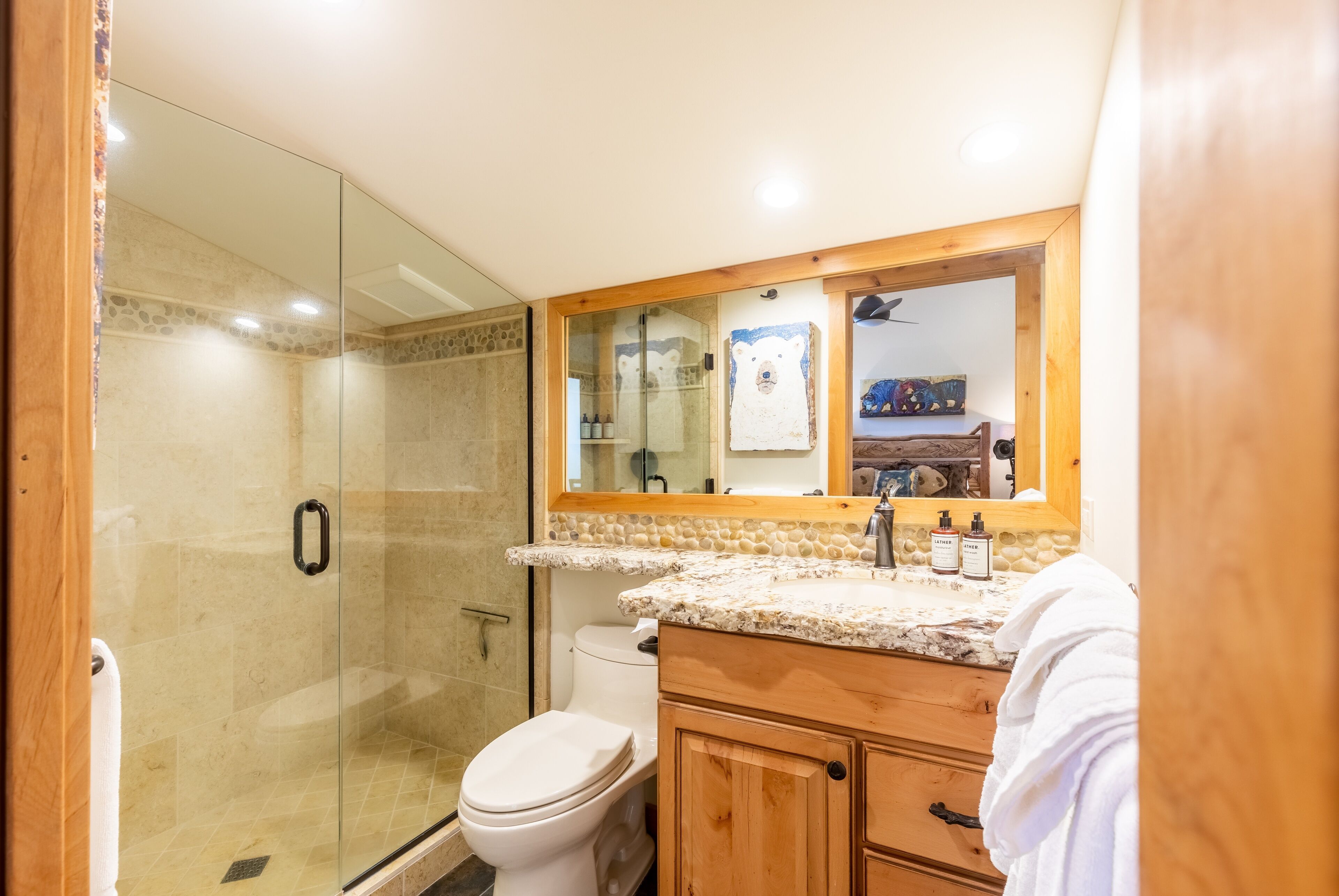 A bathroom with a glass-enclosed shower, a toilet, wooden cabinets, and a marble countertop.