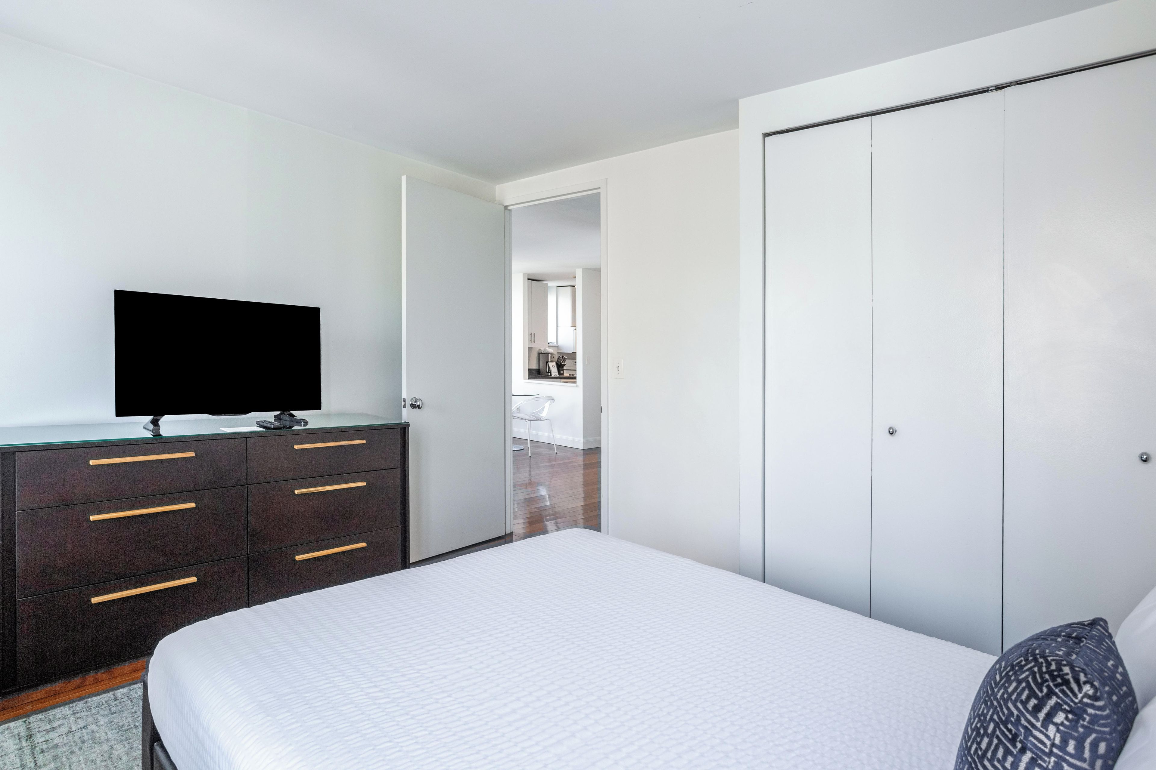 A bedroom with a bed, a dresser with drawers, a television on top, and a wardrobe.