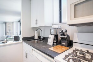 A modern kitchen with white cabinets, a stainless steel sink, a coffee maker, and a gas stove.