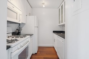 A compact kitchen with white cabinets, a stove, a refrigerator, and a sink.