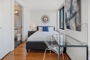 A modern bedroom with a bed, bedside table, and a glass desk.