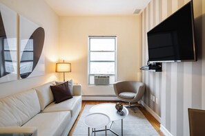 Een moderne woonkamer met een witte bank, een ronde salontafel, een lamp, een stoel en een flatscreen televisie aan de muur.