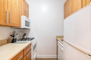 A narrow kitchen with wooden cabinets, a microwave, a stove, and a dishwasher. - Timeless NYC Stay | UES | Pet Friendly (New York)