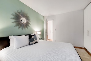 A bedroom with a large bed, a mirror with a sunburst design, a nightstand with a lamp, and a wardrobe.