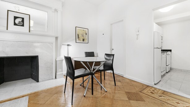 Un'elegante zona pranzo con camino in marmo, un tavolo rotondo con sedie e una cucina con elettrodomestici bianchi.