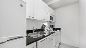 Una cucina moderna con mobili bianchi, un piano di lavoro nero, elettrodomestici in acciaio inossidabile e un forno a microonde sopra il piano cottura.
