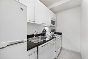 A modern kitchen with white cabinetry, a black countertop, stainless steel appliances, and a microwave above the stove.