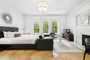 A modern bedroom with a large bed, a sofa, a TV, and a fireplace. - Classic UWS Living | Riverside Park | Pet-Friendly (New York)