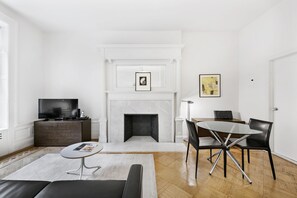 A modern living room with a fireplace, a dining table with chairs, a sofa, and a television on a cabinet. - Classic UWS Living | Riverside Park | Pet-Friendly (New York)