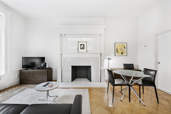 A modern living room with a fireplace, a dining table with chairs, a sofa, and a television on a cabinet.