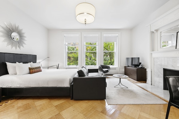 A modern bedroom with a large bed, a sofa, a TV, and a fireplace.