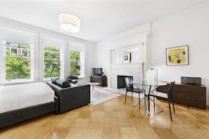 A modern hotel room with a large bed, a sofa, a dining table, and a fireplace.