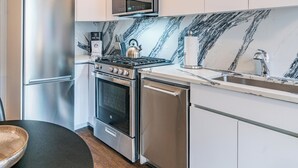 Een moderne keuken met roestvrijstalen apparatuur, een marmeren spatwand en witte kasten.
