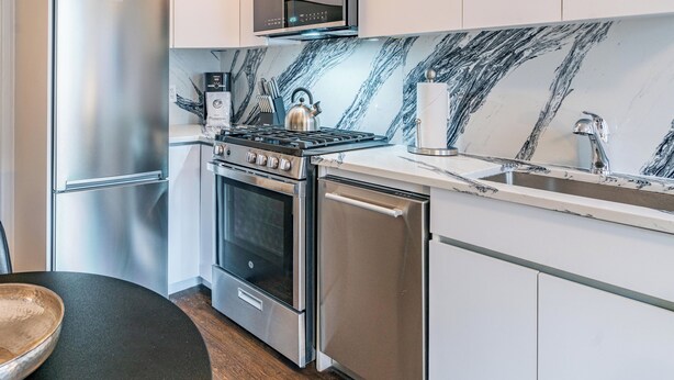 A modern kitchen with stainless steel appliances, a marble backsplash, and white cabinetry. - Classic NYC Living | UES, Pet-Friendly (New York)